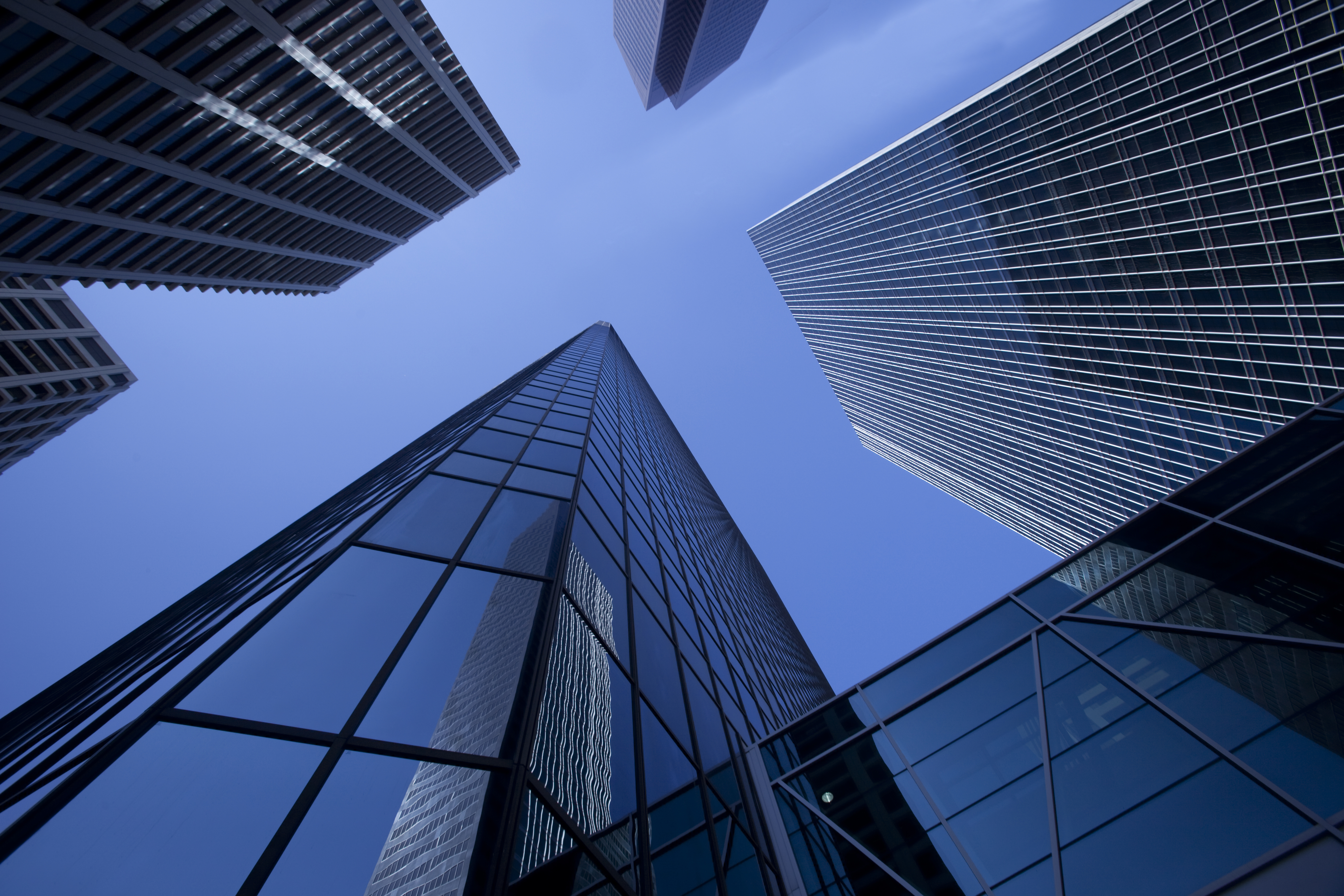 Tall modern skyscrapers with a jumbo jet passing over leaving a sharp contrail.